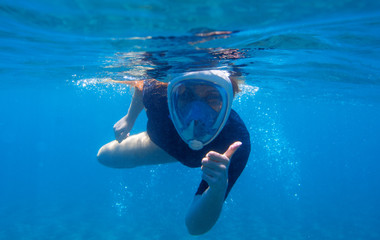 Woman snorkeling undersea portrait. Snorkel shows thumb up underwater. Happy woman snorkeling in...