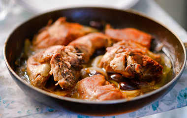 Fried rabbit legs on frying pan with vegetables and herbs