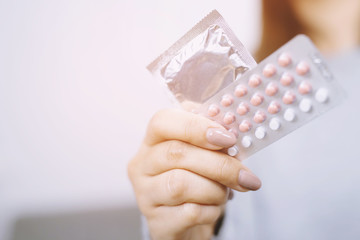 Contraceptive means: Woman hand holding contraceptive pills and condom sitting on sofa background. Protection, safe sex. Contraception, concept birth control. Copy space
