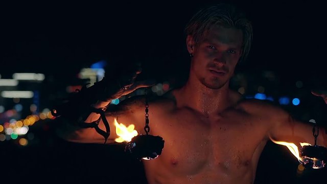 Young blond male lowers two burning pois hanging on chains. Slow motion shot. Close-up