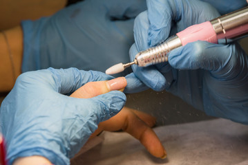 Fototapeta premium The manicurist processes old gel varnish a mill