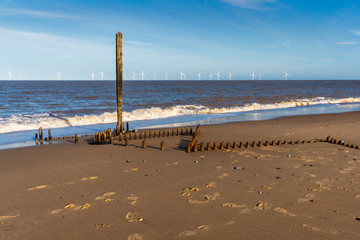 North sea coast in Caister-on-Sea, Norfolk, England, UK - with the remains of a wave breaker at the beach and wind turbines in the background