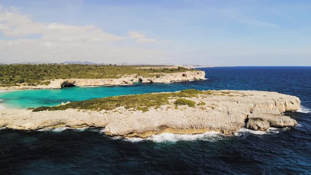 a drone shot flying towards a rocky outcrop next to a beach called cala varques in majorca