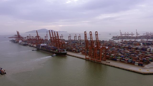 Drone shoot of landscape in Shenzhen,China.Cargo terminal full of containers,many cranes in the dock.Barges parked on smooth sea surface under cloudy sky.