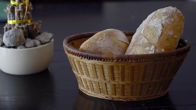 a basket of crusty sourdough bread and a flower pot against a black background.