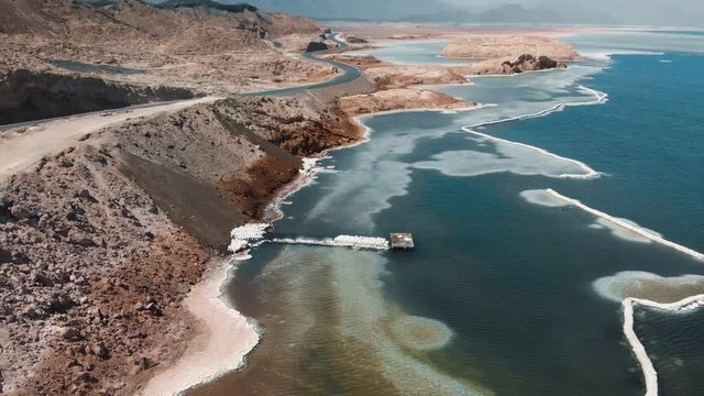 Aerial of Salt Lake Assal Djibouti Africa Volcanic Area - Crystal Blue Water and Rocky Hills Desert - Cinematic Footage 4K Backward Reveal Opener Shot