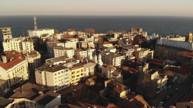 Pan aerial shot of Old Town Constanta City and harbor, Romania, Europe. Shot in spring during sunset and Golden Hour, revealing the Black Sea and the architecture while seagulls fly
