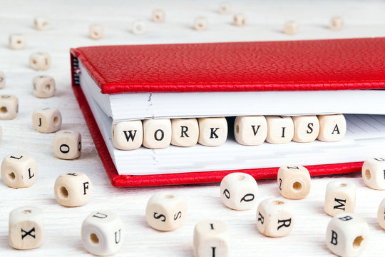 Phrase Work visa written in wooden blocks in red notebook on white wooden table.