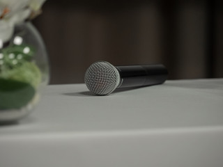 Fototapeta premium On the table lies a black-and-white microphone. Partially visible bouquet of white orchids in a glass vase on the table