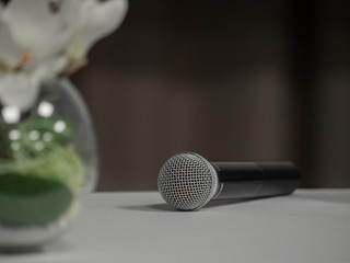 Obraz premium On the table lies a black-and-white microphone. Partially visible bouquet of white orchids in a glass vase on the table