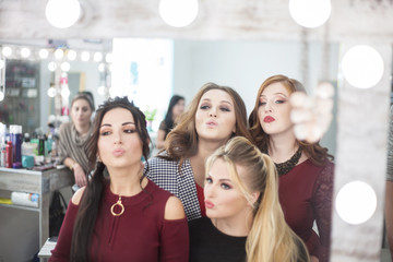 Fototapeta premium Four young women looking in the mirror in the beauty salon.