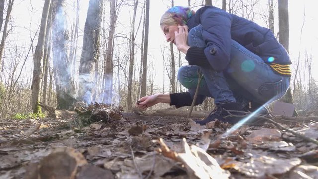 A woman inflames a kosyutr in the autumn forest, puts dry leaves to ignite, blows it to inflame