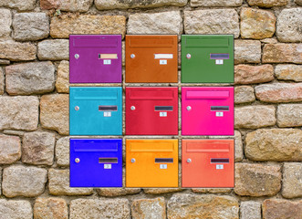 Incrustation de boîtes aux lettres couleurs dans mur de pierres 