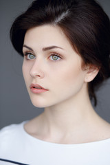 Naklejka premium A sensual brunette with clean skin, special features, ponytail and green eyes look thoughtfully at the one side.Vertical view on gray background.