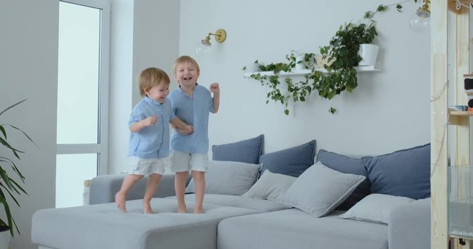 Two brothers of little boys are jumping on the couch and having fun. Joy, laughter and fun at home. Happy childhood