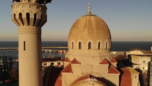 Lift drone movement of the Kral Cami King's Islam mosque in Old Town area of Constanta City, Romania, in eastern Europe  revealing the Black Sea in the background while birds fly around.