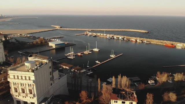Pan aerial shot of Old Town Constanta City and harbor, Romania, Europe. Shot in spring during sunset and Golden Hour, revealing architecture, boats and coastline,  while seagulls fly