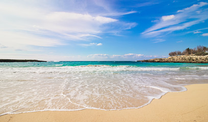 Fototapeta na wymiar Salento beach, Taranto, Puglia, Italy, waves breaking on the coast and isolated stones on the sand, partly cloudy blue sky