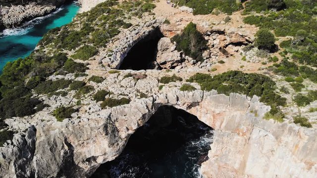 a drone shot flying backwards away from a sea arch near cala varques in majorca.