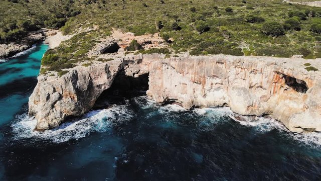 a wide drone shot flying upward of a large sea arch near cala varques in majorca