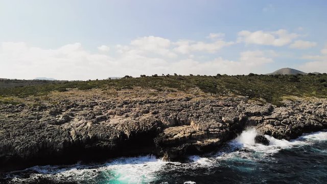 a drone shot rotating to show waves splashing onto a rocky shore and spraying into the air near cala varques in majorca