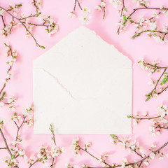 Flower frame with white flowers and paper vintage card on pink background. Flat lay