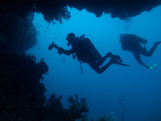 Two divers are silhouetted through cave and coral