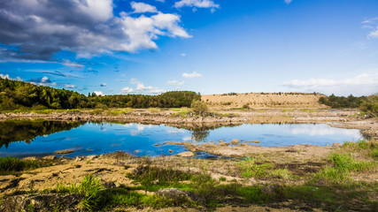 Obraz premium Sandy hills. Lake in the Sandy canyon. Warm colors background. Yellow sandstone textured mountain, white thin sand dune, bright sky. Sunshine landscape