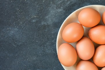 a beige plate with orange and yellow fresh eggs stands on a dark background of dark blue cement with free space on the left