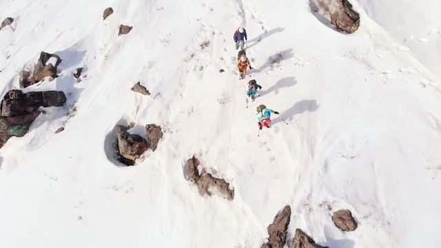 four tourists climb the mountain, helping themselves with ski poles. aerial Shot with quadcopter rotating camera.