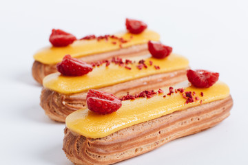 Set of delicious eclairs with yellow glaze and raspberries