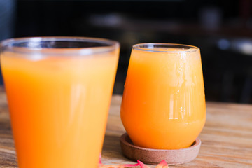 A glasses of ice orange juice on wooden table with maple leaf