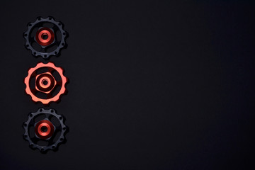 Color rollers, black, red gears for bicycle rear derailleur on black background in left side, with copyspace