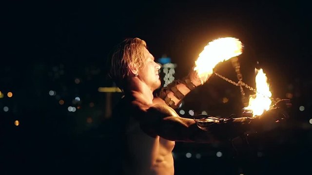 Young blond male spins two burning pois tied together. Slow motion shot. Close-up