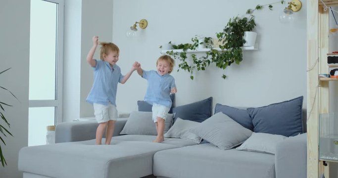 Two little boys jumping on the couch and having fun. Joy, laughter and fun at home