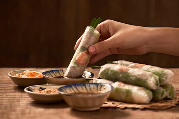 Hand dipping vegetarian rice paper rolls into the soy sauce