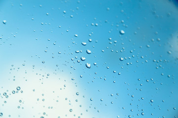 Water drops on the window, blue sky and clouds in the blurry background.