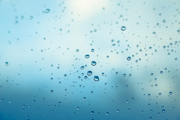 Water drops on the window, blue sky and clouds in the blurry background.