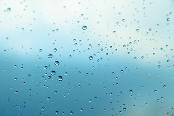 Water drops on the window, blue sky and clouds in the blurry background.