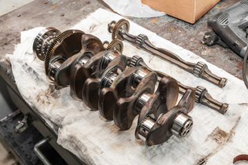 Close-up of a car crankshaft removed for replacement on a workbench in a vehicle repair shop. Auto service industry.