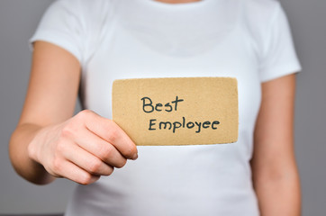 Best Employee concept   phrase handwritten  on square  cardboard paper holding by young caucasian  women  in  right hand.