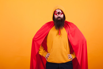 Handsome bearded man in superhero costume standing proudly over yellow background