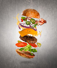 Tasty cheeseburger with flying ingredients on dark background. High resolution image.