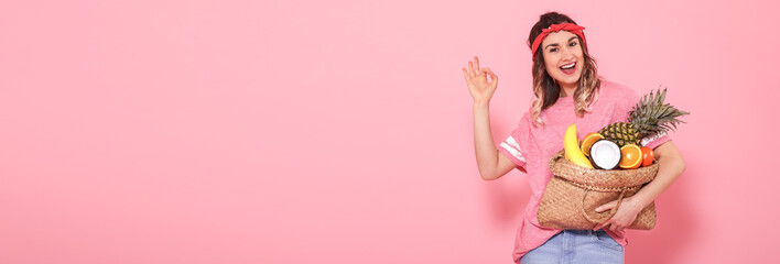 Beautiful young girl in pink t-shirt, holds a full straw bag of fruit on pink background