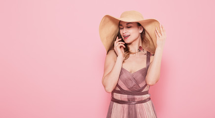 Portrait of a girl in a summer hat and dress on a pink background