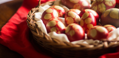 Traditional red Easter eggs with rose leaf, in basket on wood background. 