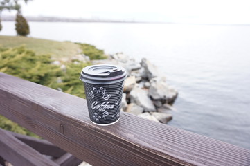 Cardboard disposable cup of coffee is on the fence of the bridge. Walk in nature.