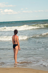 A girl stands in front of the blue soft waves of the sea. Summer, vacation and relax on the beach of ocean.