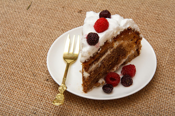 Slice of homemade biscuit cake decorated with whipped cream and raspberries.