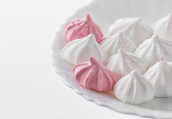 White-pink meringues on a white plate on a white background. 